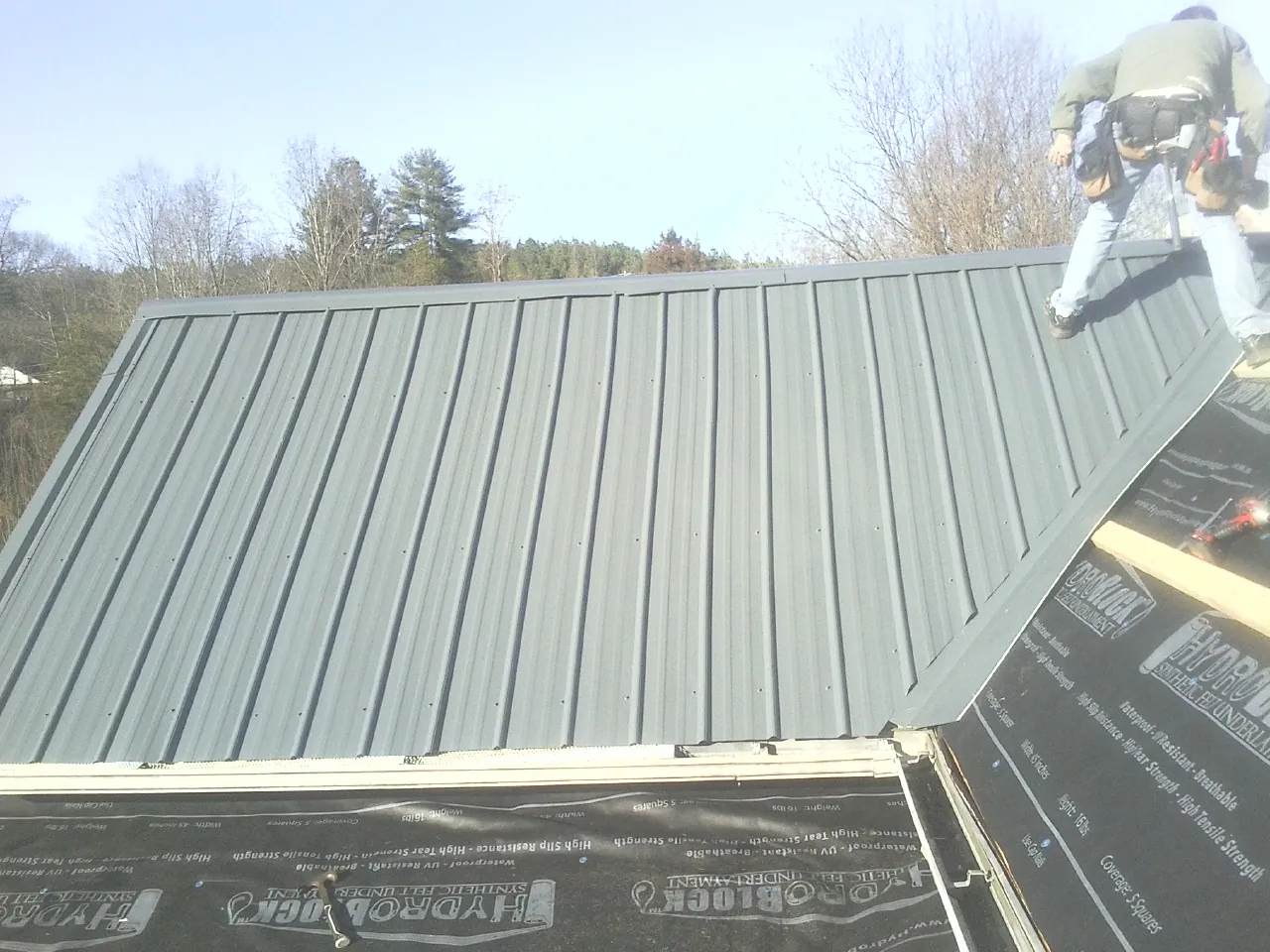 Crew installing dark green standing seam panels over synthetic underlayment in Oneonta