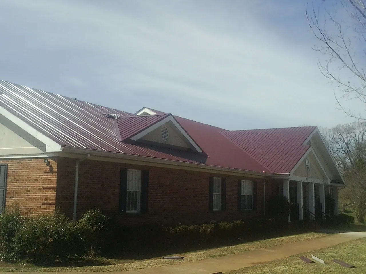 Red metal roof with gabled entries on a long brick building, from a Hail Damage Roof Repair job in Oneonta