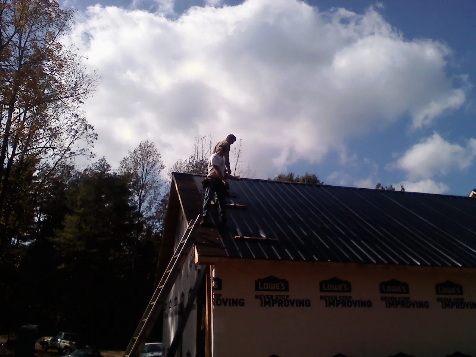 Roofer fastening dark metal panels high against a cloudy sky, from a Roof Inspection job in Oneonta