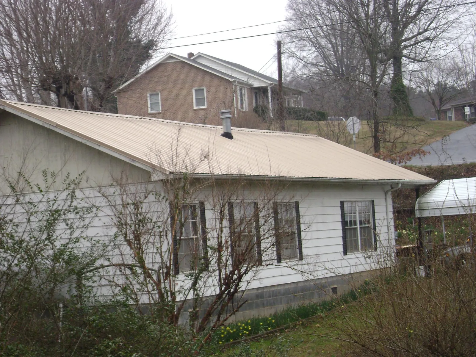 Tan metal roof on a white sided house set into a hillside — Commercial Roofing by Roofing Brothers in Oneonta