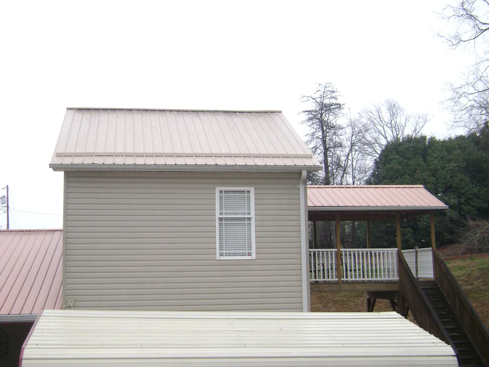 Tan metal roofs on a two story addition and attached porch, from a Roof Replacement job in Oneonta